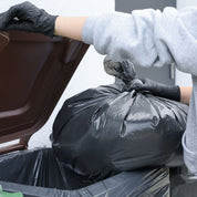 Person wearing gloves placing a black trash bag into a car trunk.