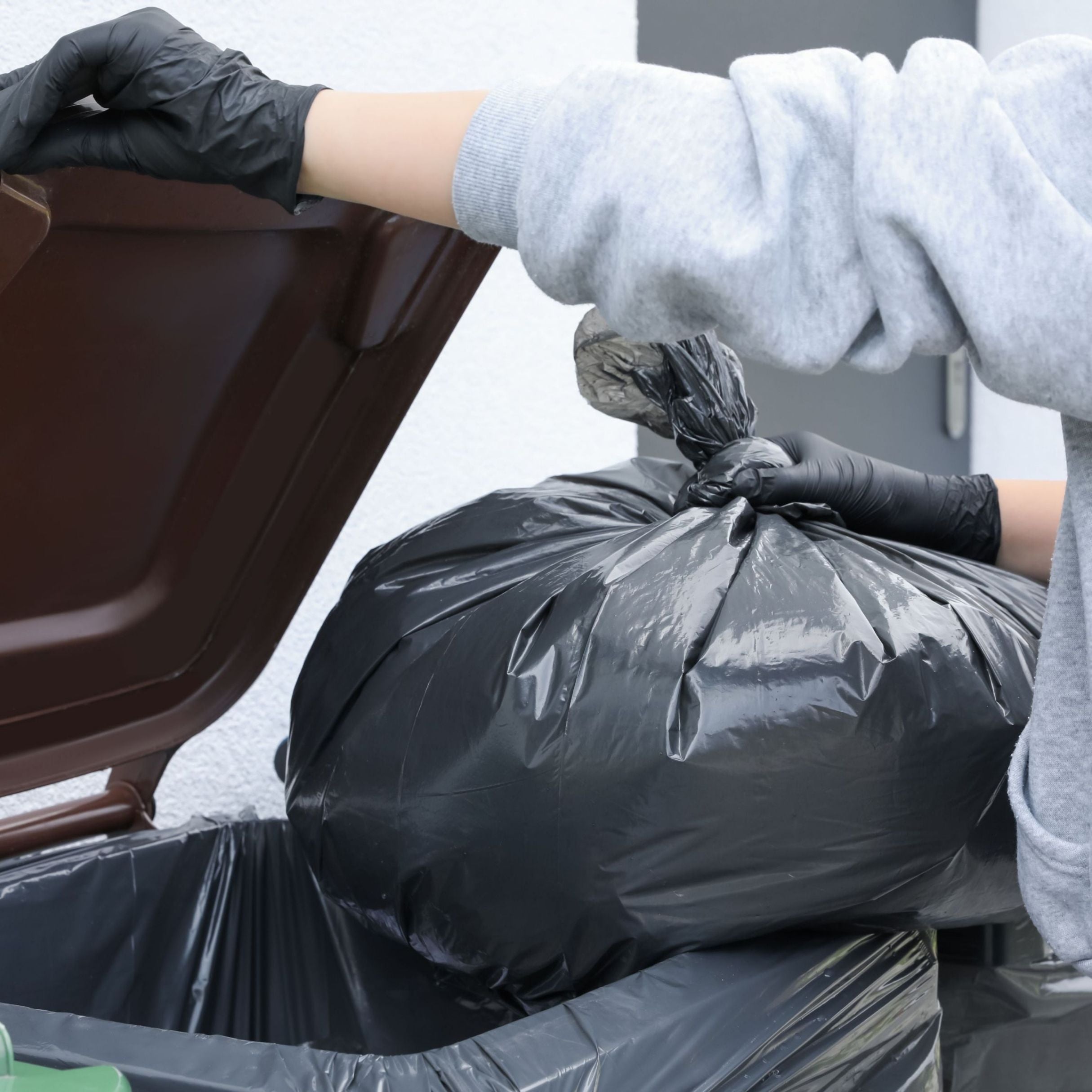 Person wearing gloves placing a black trash bag into a car trunk.